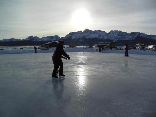 A person ice skating on a frozen lake with mountains and a sunset in the background.
