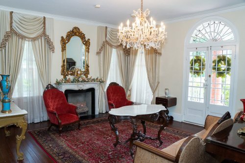 Elegant living room with red chairs, a chandelier, and a decorative mirror, featuring a fireplace and large windows.