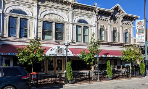 Exterior of The Blue Moon restaurant, featuring a red awning and decorative architecture, with trees and a clear blue sky.