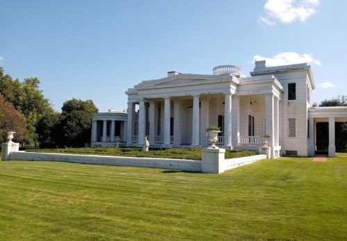 A grand white mansion with columns, surrounded by green lawns and blue skies.