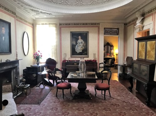 A vintage room with ornate decor, featuring a large painting, elegant furniture, and a patterned rug.