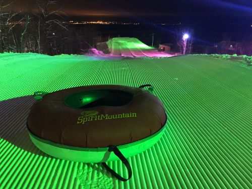 A snow-covered slope at night, illuminated with green lights, featuring a red snow tube at the foreground.