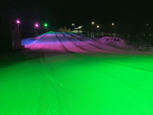 A snow-covered slope illuminated by colorful lights in a nighttime setting.