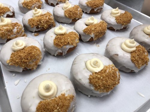 A tray of donuts topped with white icing, crumbled graham crackers, and a swirl of cream.