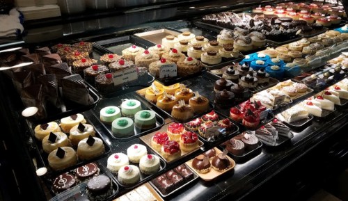 A display case filled with a variety of colorful cakes and pastries, topped with cherries and chocolate decorations.