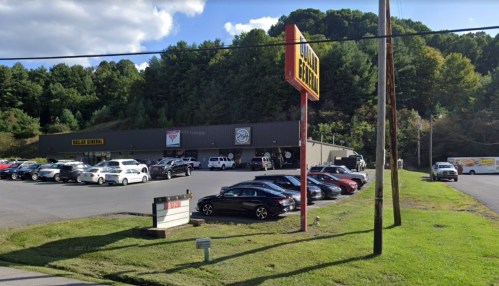 A parking lot filled with cars in front of a large building surrounded by trees under a blue sky.