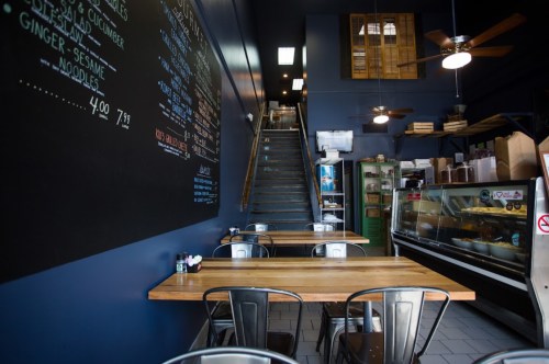 Interior of a cozy restaurant featuring wooden tables, a chalkboard menu, and a staircase leading to an upper level.