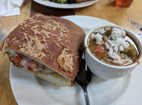 A plate with a crusty sandwich and a bowl of gumbo with rice, garnished with vegetables.