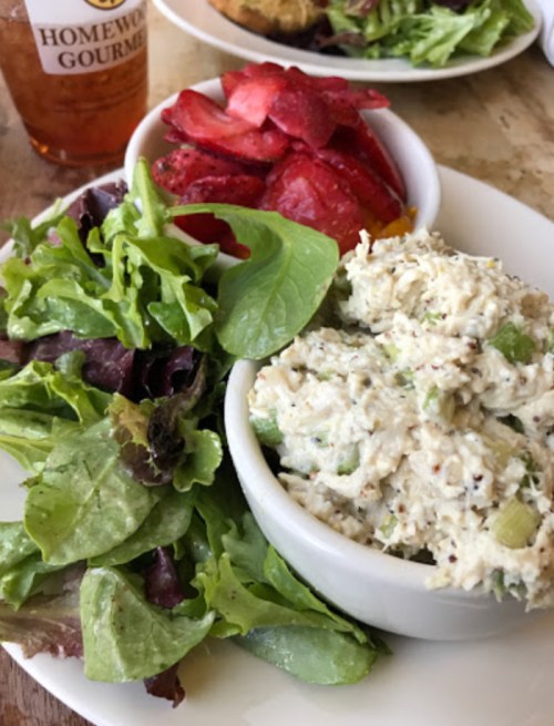 A plate featuring a bowl of chicken salad, mixed greens, and a side of strawberries.