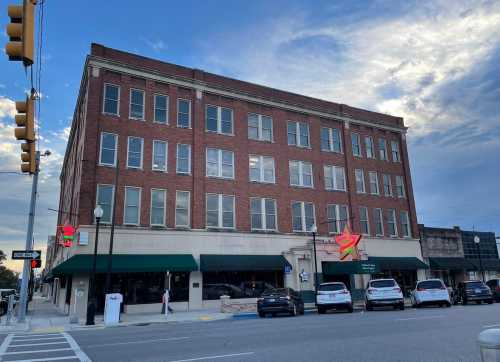 A historic brick building with large windows, green awnings, and street parking under a blue sky with clouds.