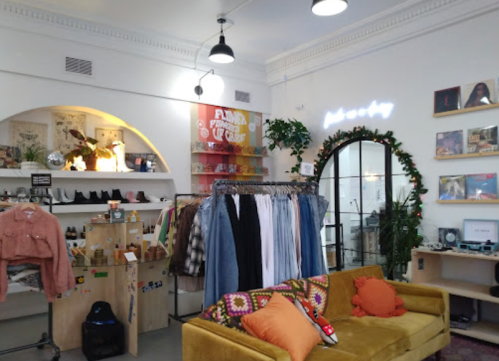 A cozy boutique interior featuring clothing racks, a yellow sofa, and decorative wall art.
