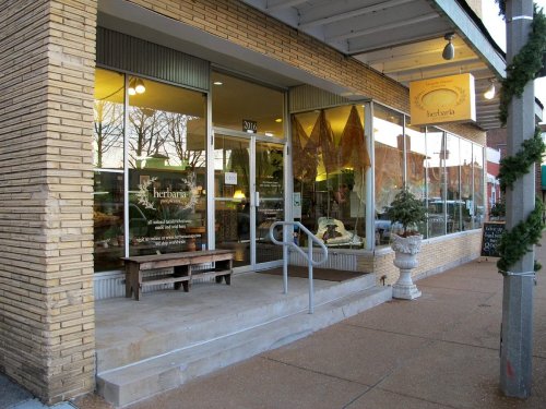 A storefront with large windows displaying decorative items, featuring a bench outside and a welcoming entrance.