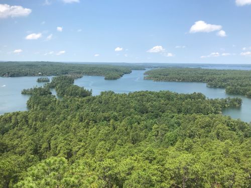 Aerial view of a lush green landscape with a winding lake and islands under a clear blue sky.