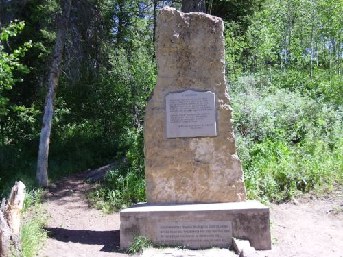 A large stone monument surrounded by trees, featuring an engraved plaque with text.