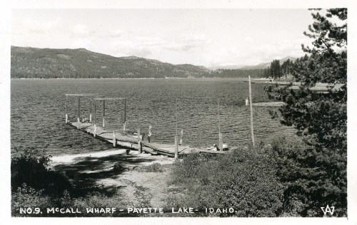 Black and white photo of McCall Wharf at Payette Lake, Idaho, featuring a wooden dock and scenic mountains in the background.