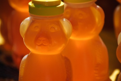 Close-up of honey bottles shaped like bears, with yellow caps and a warm amber color.