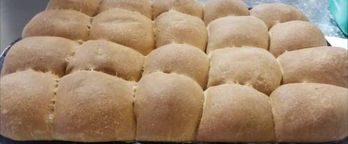 Freshly baked whole wheat dinner rolls arranged in a rectangular tray, golden brown and fluffy.