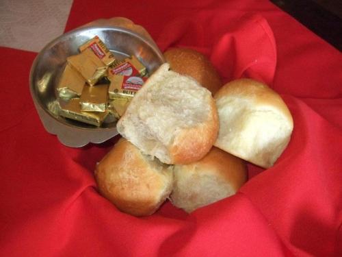 A silver bowl with butter packets beside a pile of soft, golden dinner rolls on a red cloth.