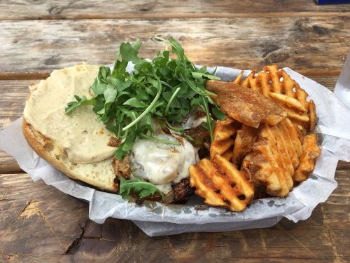 A sandwich with melted cheese and greens, served with crispy waffle fries on a wooden table.