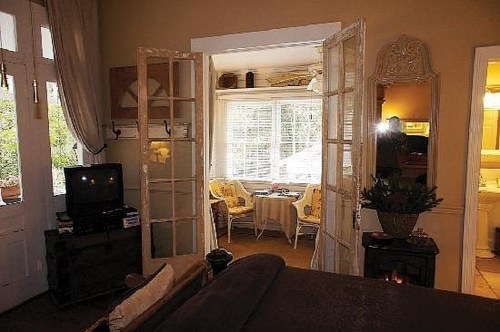 Cozy room with open French doors leading to a sunlit dining area with a table and chairs.