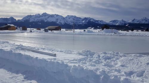 A snowy landscape with a frozen surface and mountains in the background under a cloudy sky.