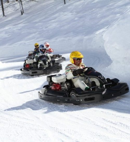 Four go-karts racing on a snowy track, with drivers wearing helmets and winter gear.