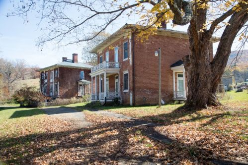 Two brick houses with white trim, surrounded by autumn leaves and trees, under a clear blue sky.