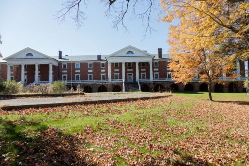 Historic building with columns, surrounded by autumn leaves and trees, under a clear blue sky.