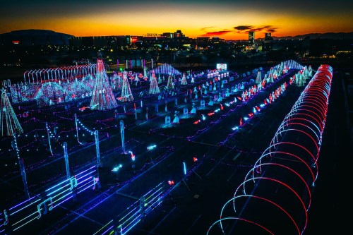 Aerial view of a vibrant holiday light display with colorful patterns against a sunset backdrop.