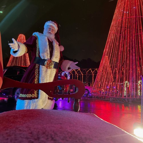A festive Santa Claus stands in front of colorful holiday lights, with a snowy night backdrop.