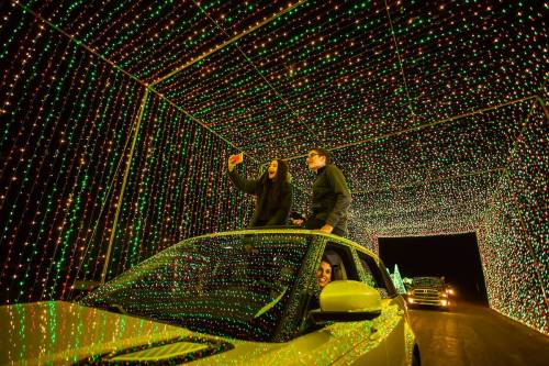 A car with three people inside is surrounded by colorful holiday lights in a festive tunnel.