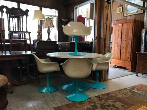 A retro dining set featuring a round table and four chairs with white seats and turquoise bases in a vintage shop.
