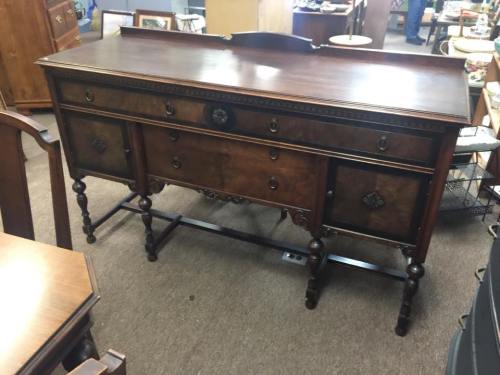 A vintage wooden sideboard with multiple drawers and ornate detailing, set in a furniture store.