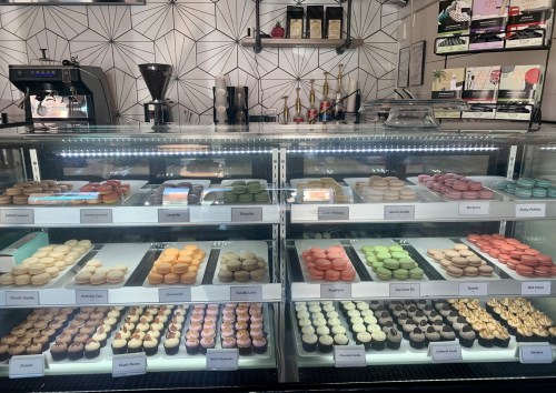 A display case filled with colorful macarons and cupcakes in a modern café setting.