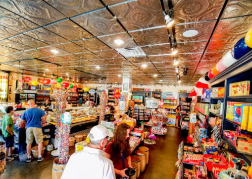 A colorful candy store interior with shelves filled with sweets and customers browsing. Bright decor and a shiny ceiling.