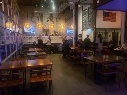 Interior of a lively restaurant with wooden tables, hanging lights, and patrons enjoying their meals.