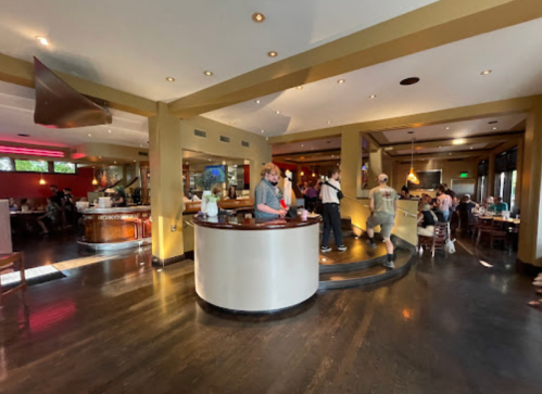 A modern restaurant interior with a bar area, patrons dining, and staff interacting in a warm, inviting atmosphere.