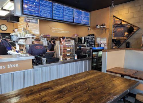 A cozy restaurant interior with a wooden table, counter, menu boards, and staff preparing food in the background.