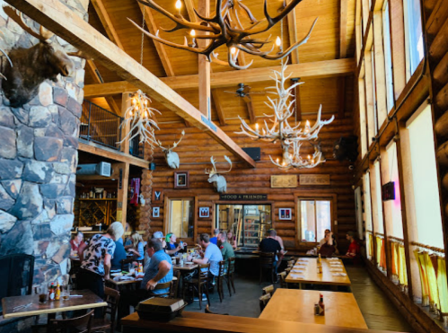 A rustic restaurant interior with wooden beams, antler decor, and diners enjoying meals at wooden tables.