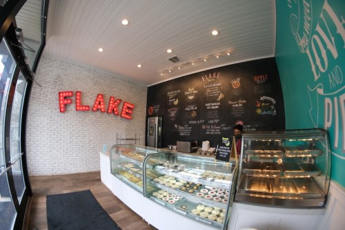 Interior of a bakery named "Flake," featuring a display case of desserts and a chalkboard menu on the wall.