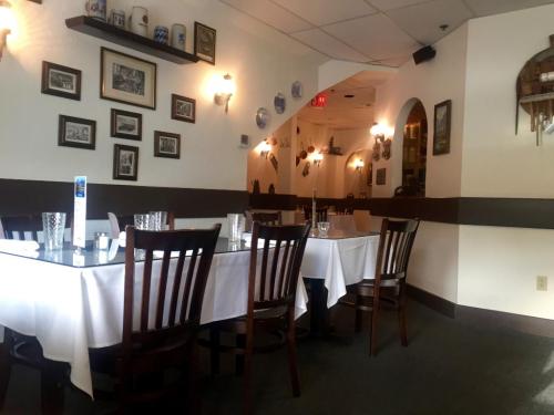 A cozy restaurant interior with white tablecloths, wooden chairs, and framed pictures on the walls.