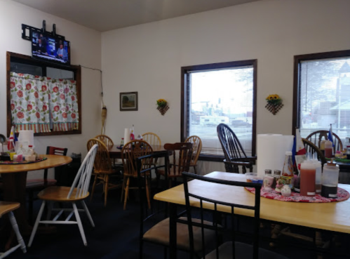 Cozy dining area with wooden tables and chairs, a TV, and decorative curtains, featuring a view of the outside.