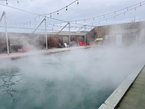 A misty outdoor pool surrounded by chairs and string lights, creating a serene and relaxing atmosphere.