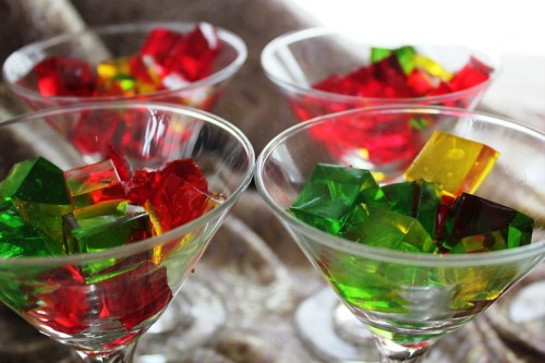 Four glass bowls filled with colorful red, green, and yellow jelly cubes on a textured surface.
