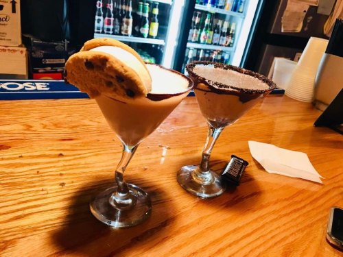 Two dessert cocktails on a bar counter, one topped with a cookie and the other with a chocolate rim.