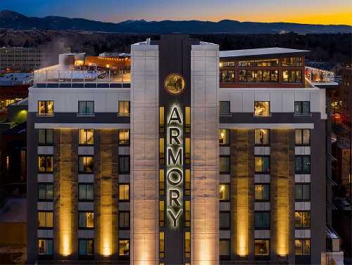 A modern hotel building at dusk, featuring the name "ARMORY" prominently displayed, with a rooftop terrace and mountain backdrop.