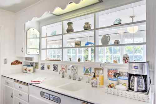 Bright kitchen with white countertops, a double sink, and shelves displaying various decorative items and dishes.