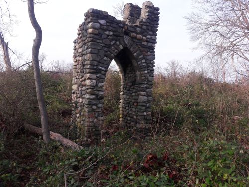 A stone archway stands amidst overgrown vegetation and trees, hinting at a forgotten structure in nature.