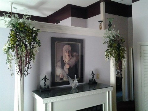 A cozy room with a fireplace, adorned with floral arrangements and a framed portrait above the mantel.