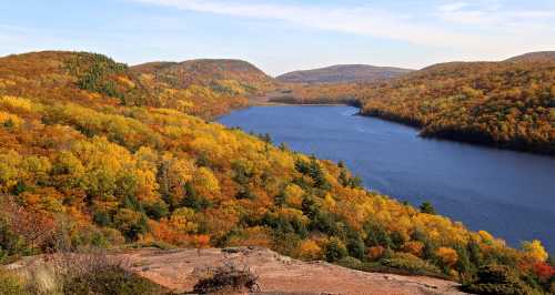 A scenic view of a lake surrounded by vibrant autumn foliage and rolling hills under a clear blue sky.